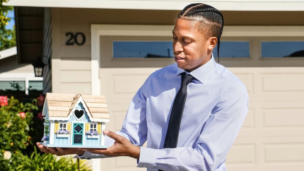 A real estate agent presenting a miniature house model in front of a residential property.