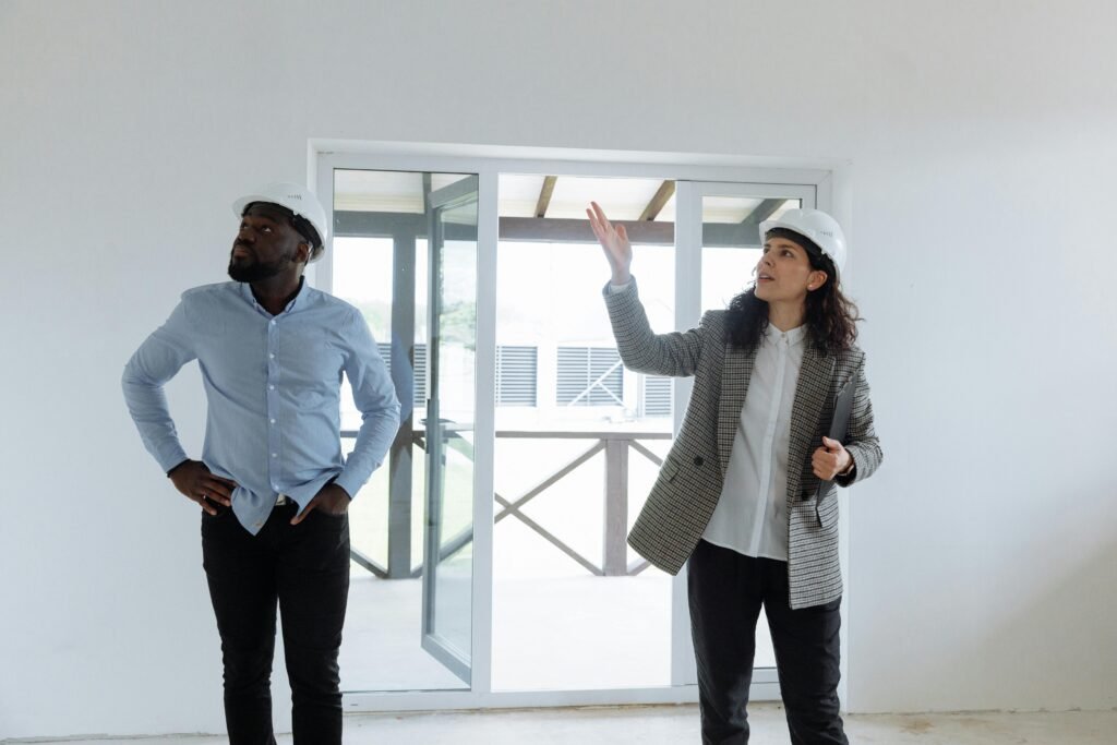 Two contractors inspecting a modern house interior wearing hard hats.